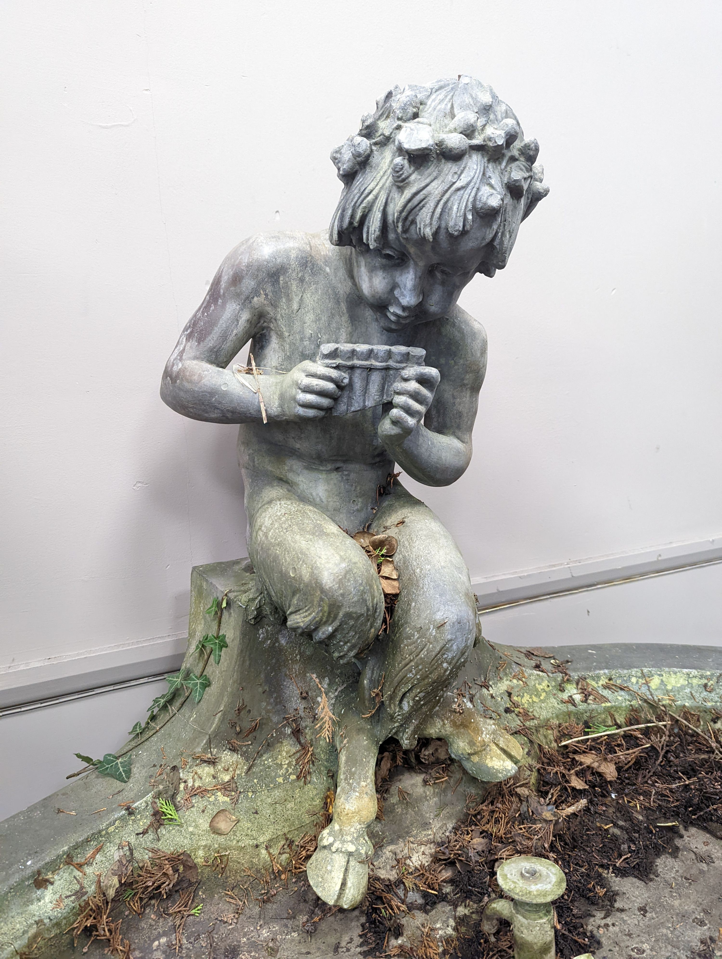 An early 20th century oval lead garden fountain formed as a seated satyr playing pan pipes with stylised dolphin spout, width 120cm, depth 84cm, height 74cm
